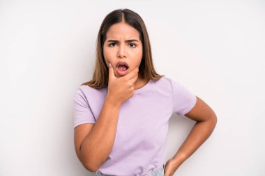 hispanic latin pretty woman with mouth and eyes wide open and hand on chin, feeling unpleasantly shocked, saying what or wow