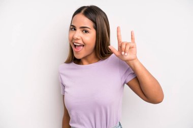 hispanic latin pretty woman feeling happy, fun, confident, positive and rebellious, making rock or heavy metal sign with hand