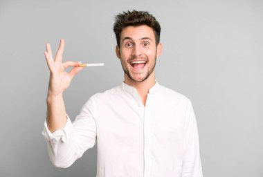 Genç ve yakışıklı bir adam izole edilmiş ve elinde sigara tutuyor.