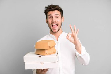 Fast food ile izole edilmiş genç yakışıklı adam kutuları taklit ediyor. teslimat ve paket konsepti