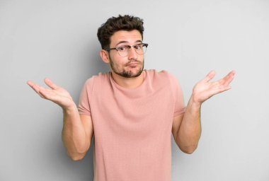 Genç yakışıklı adam şaşkın ve şaşkın, şüpheci, farklı seçenekleri tartıyor ya da komik bir ifadeyle seçiyor.