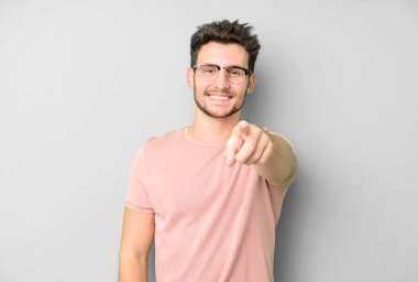 Genç ve yakışıklı bir adam kameraya bakıyor. Tatmin olmuş, kendine güvenen, dost canlısı bir gülümsemeyle seni seçiyor.