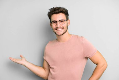 Genç yakışıklı adam kendini mutlu ve neşeli hissediyor, gülümsüyor ve seni selamlıyor, dostça bir jestle içeri davet ediyor.