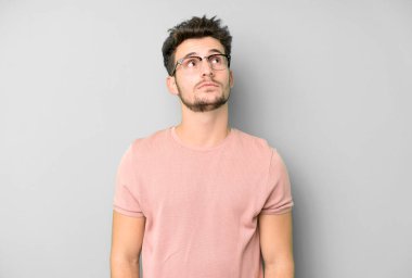 Endişeli, kafası karışık, budala bir ifadeyle genç yakışıklı adam, kopya alanı arıyor, şüphe ediyor.