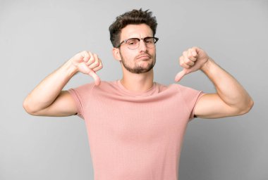 Genç yakışıklı adam üzgün, hayal kırıklığına uğramış ya da kızgın görünüyor, anlaşmazlık içinde baş parmağını gösteriyor, hayal kırıklığına uğramış hissediyor.