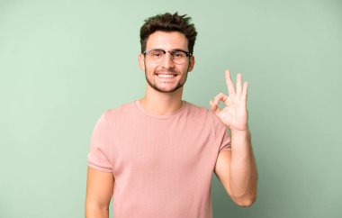 Genç yakışıklı adam mutlu, rahat ve tatmin olmuş hissediyor. Onayını iyi bir hareketle gösteriyor. Gülümsüyor.