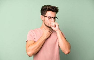 Gırtlağı ağrıyan, grip semptomları gösteren, ağzı kapalı öksüren genç yakışıklı bir adam.