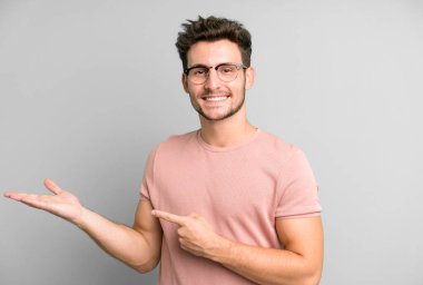 Genç yakışıklı adam gülümsüyor, mutlu, tasasız ve tatmin olmuş hissediyor, fotokopi alanındaki konsepte ya da fikre işaret ediyor.