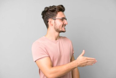 Genç yakışıklı adam gülümsüyor, seni selamlıyor ve başarılı bir anlaşma için el sıkışmayı teklif ediyor.