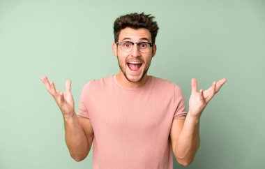 Genç yakışıklı adam mutlu, heyecanlı, şaşırmış ya da şok olmuş hissediyor, gülümsüyor ve hayrete düşüyor.
