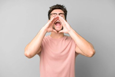 Genç yakışıklı adam mutlu, heyecanlı ve pozitif hissediyor. Elleri ağızda, bağırıyor.