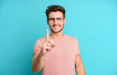 Genç ve yakışıklı bir adam gururla gülümsüyor ve gururla bir numaralı pozu veriyor, kendini lider gibi hissediyor.