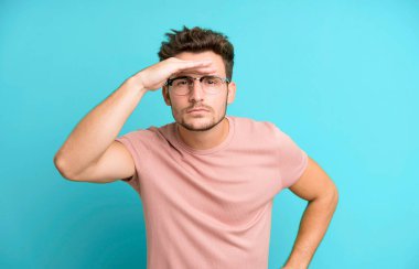 Genç yakışıklı adam şaşkın ve şaşkın bakıyor, el üstünde uzak bakıyor, izliyor ya da arıyor