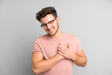 Genç yakışıklı adam üzgün, yaralı ve kalbi kırık görünüyor, iki elini de kalbine yakın tutuyor, ağlıyor ve bunalımda.