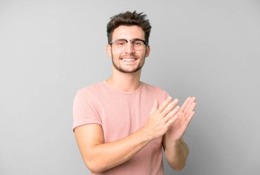 Genç yakışıklı adam kendini mutlu ve başarılı hissediyor, gülümsüyor ve alkışlıyor, alkışlarla tebrik ediyor.