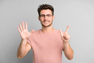 Genç yakışıklı adam gülümsüyor ve dost canlısı görünüyor, 7 ya da 7 numarayı gösteriyor, eli önde, geriye doğru sayıyor.