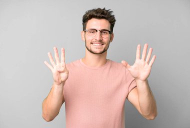 Genç yakışıklı adam gülümsüyor ve arkadaş canlısı görünüyor. 9 ya da 9 numarayı gösteriyor. Elleri önde, geriye doğru sayıyor.