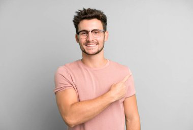 Genç yakışıklı adam neşeyle gülümsüyor, mutlu hissediyor ve kenarı ve yukarıyı işaret ediyor, fotokopi uzayındaki nesneleri gösteriyor.