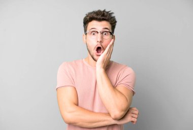 Genç yakışıklı adam şok ve inançsızlık içinde, elleri yanak ve kolları çapraz, sersemlemiş ve şaşırmış hissediyor.