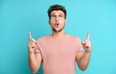 Genç yakışıklı adam şaşırmış, şaşırmış ve ağzı açık, iki eliyle uzayı göstererek