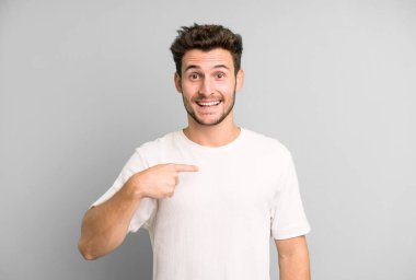 Genç yakışıklı adam mutlu, gururlu ve şaşırmış görünüyor, neşeli bir şekilde kendini gösteriyor, kendinden emin ve yüce hissediyor.