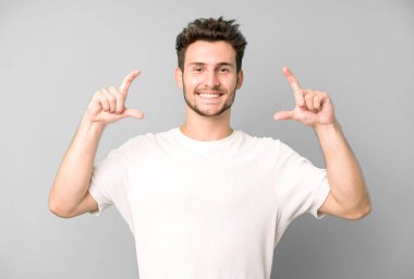 Genç yakışıklı bir adam kendi gülüşünü çiziyor ya da özetliyor iki eliyle, pozitif ve mutlu görünüyor, sağIık kavramı.