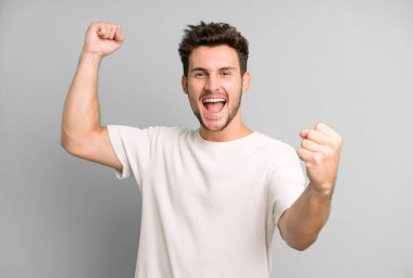 Genç yakışıklı adam zaferle bağırıyor. Heyecanlı, mutlu ve şaşırmış görünüyor. Kutlama yapıyor.