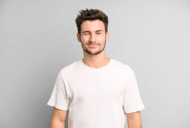 Genç yakışıklı adam mutlu ve arkadaş canlısı görünüyor, gülümsüyor ve sana olumlu bir tavırla göz kırpıyor.