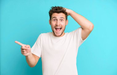 Genç yakışıklı adam gülüyor, mutlu, pozitif ve şaşırmış görünüyor. Yan fotokopi alanını işaret eden harika bir fikrin farkına varıyor.