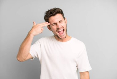 Genç yakışıklı adam mutsuz ve stresli görünüyor, intihar jesti silahla işaret ediyor, kafasını işaret ediyor.