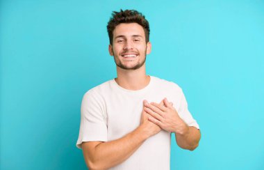 Genç yakışıklı adam romantik, mutlu ve aşık, neşeyle gülümsüyor ve kalbe yakın el ele tutuşuyor.