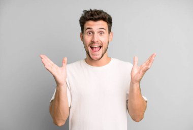 Genç yakışıklı adam mutlu ve heyecanlı görünüyor. Beklenmedik bir sürprizle şoke olmuş. İki eli yüzü açık.