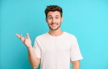 Genç yakışıklı adam kendini mutlu, şaşırmış ve neşeli hissediyor. Pozitif bir tavırla gülümsüyor. Bir çözüm ya da fikir buluyor.