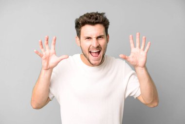 Genç ve yakışıklı bir adam panik ya da öfke içinde bağırıyor, şok olmuş, korkmuş ya da öfkeli, elleri başının yanında.