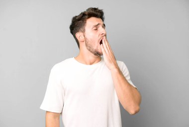 Genç yakışıklı adam tembelce esniyor, uykulu, yorgun ve sıkkın görünüyor.