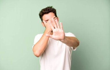 Genç ve yakışıklı bir adam elleriyle yüzünü kapatıyor ve kamerayı durdurmak için diğer elini öne koyuyor. Fotoğraf ya da resimleri reddediyor.