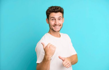 Genç yakışıklı adam neşeyle gülümsüyor ve yan taraftaki fotokopi alanını gösteriyor, mutlu ve tatmin olmuş hissediyor.