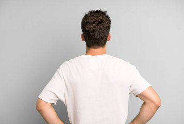 Genç, yakışıklı bir adam kafası karışık ya da dolu ya da şüphe ve soru dolu, merak ediyor, elleri kalçasında, dikiz aynasından.