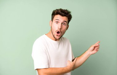 Genç yakışıklı adam şaşkın ve şaşırmış hissediyor. Kenardaki fotokopi alanını işaret ediyor. Şaşırmış, ağzı açık bir bakış.