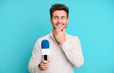 Mutlu, kendinden emin ve elleri çenesinde gülümseyen yakışıklı bir genç. Hem de mikrofonla. persenter konsepti