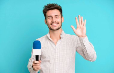 Yakışıklı genç mutlu gülümsüyor, el sallıyor, sizi selamlıyor ve selamlıyor. Hem de mikrofonla. persenter konsepti