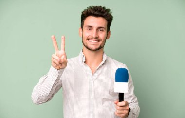 Yakışıklı genç gülümsüyor ve arkadaş canlısı görünüyor, iki numarayı gösteriyor. Hem de mikrofonla. persenter konsepti