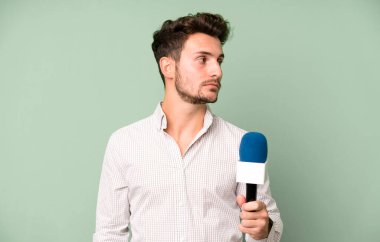 Profil görünümlü yakışıklı genç hayal kuruyor, hayal kuruyor ya da hayal kuruyor. Hem de mikrofonla. persenter konsepti