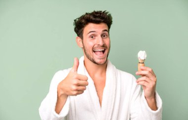Yakışıklı genç gururlu, başparmakları havada, bornoz giyiyor ve tıraş oluyor.