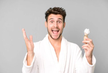 Yakışıklı genç kendini mutlu ve şaşkın hissediyor. Bornoz giyip tıraş olurken inanılmaz bir şey.