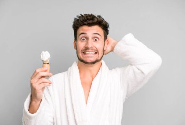 Yakışıklı genç stresli, endişeli ya da korkmuş, elleri kafasında bornoz ve traş konseptiyle