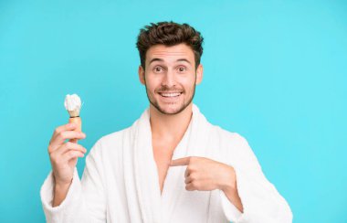 Yakışıklı genç kendini mutlu hissediyor ve heyecanlı bir bornoz giyip traş konseptiyle kendini gösteriyor.