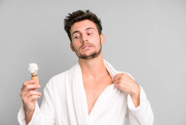 Yakışıklı genç stresli, endişeli, yorgun ve bıkkın bornoz giyiyor ve tıraş oluyor.