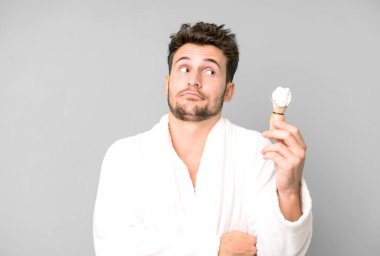 Yakışıklı genç omuz silkiyor, kafası karışık ve kararsız bornoz giyiyor ve tıraş oluyor.