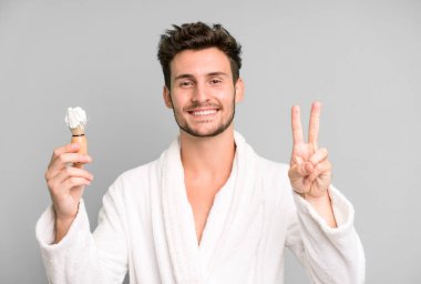 Yakışıklı genç gülümsüyor ve arkadaş canlısı görünüyor. İki numara bornoz giyiyor ve tıraş oluyor.